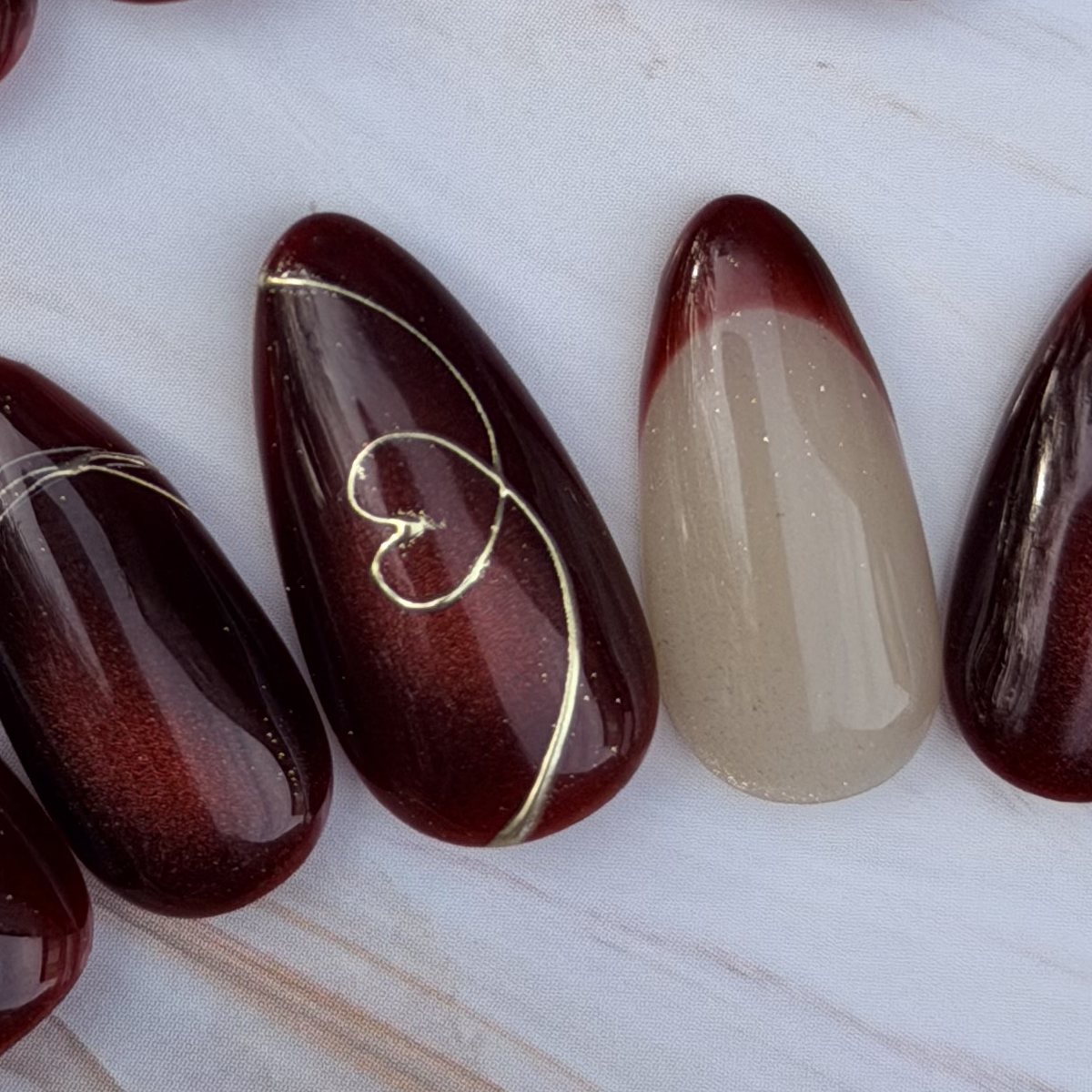 Burgundy Hearts press-on nails, close-up of the hand-painted detail