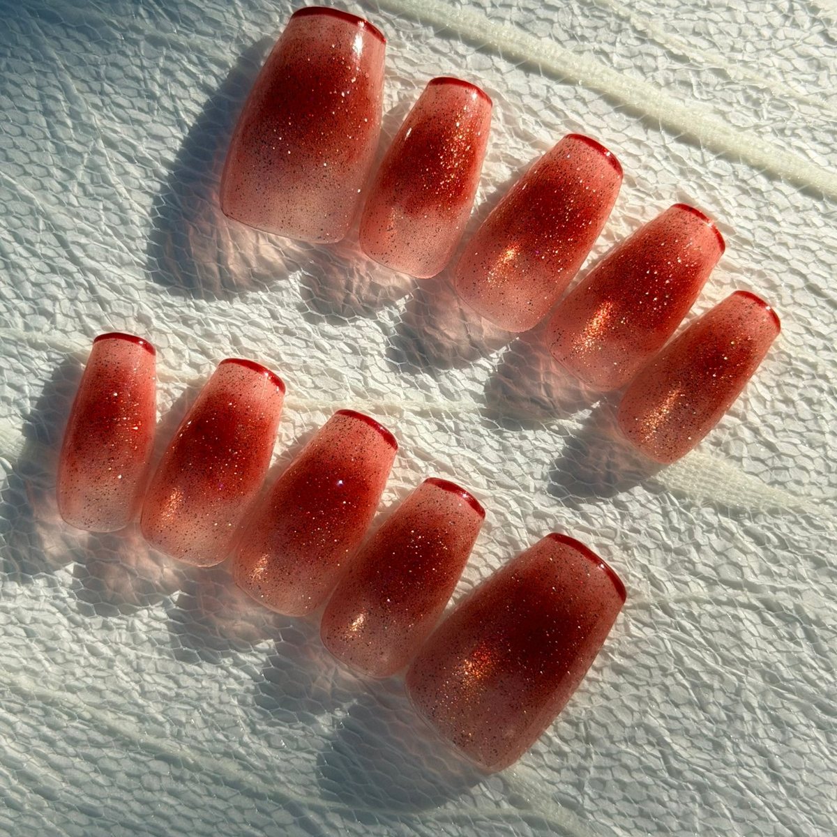 Ten medium coffin press-on nails in sheer red jelly with a glittering blush gradient and thin red French edges