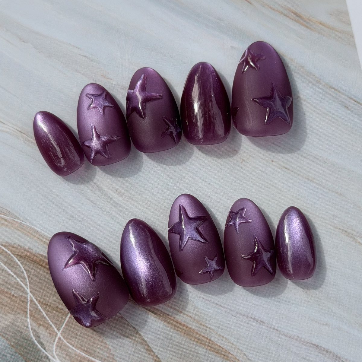 Ten almond press-on nails in violet chrome with raised three-dimensional gel stars